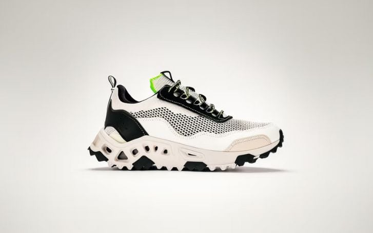 Side view of the Bio Original sneaker featuring a white and black mesh upper, chunky off-white sole with geometric cutouts, neon green tongue tab, and textured black outsole.